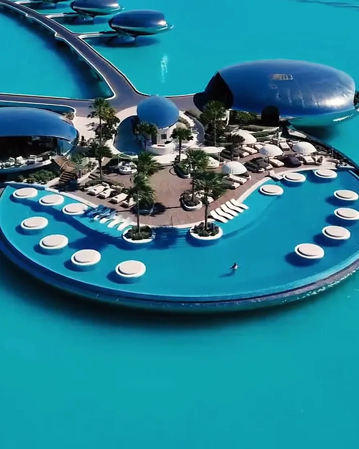 An island deck with pools and domed villas on turquoise water in the Red Sea, by day.