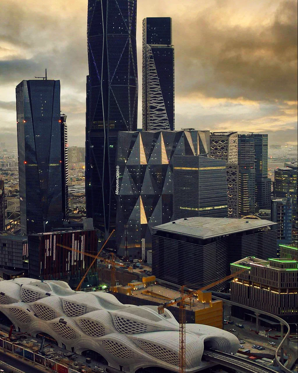 Office towers and the curved roof of a metro station under a cloudy sky.